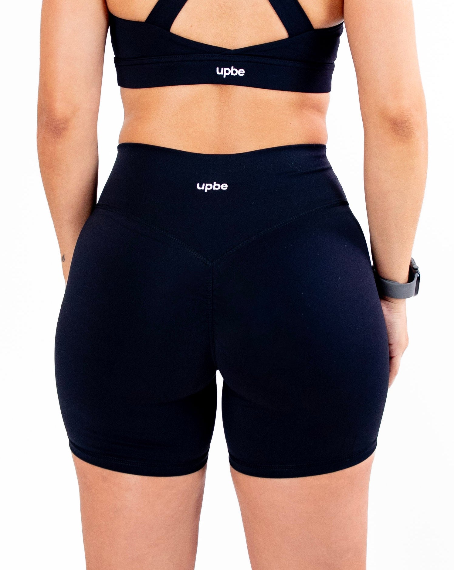 Person wearing a black sports bra and shorts with 'upbe' branding on a white background