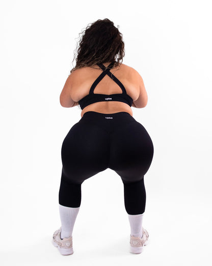 Person wearing black athletic leggings and sports bra on a white background