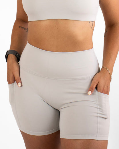 Woman wearing a grey sports bra and shorts on a white background
