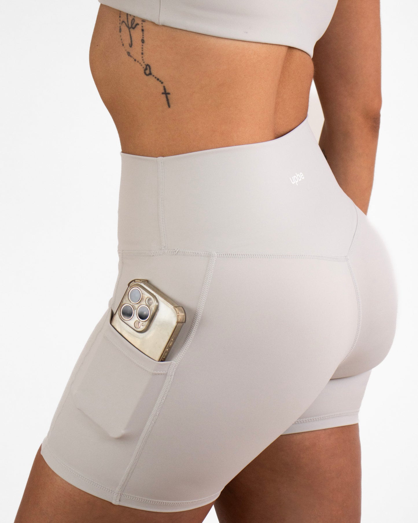 Person wearing grey high-waisted shorts with a pocket holding a phone on a plain background
