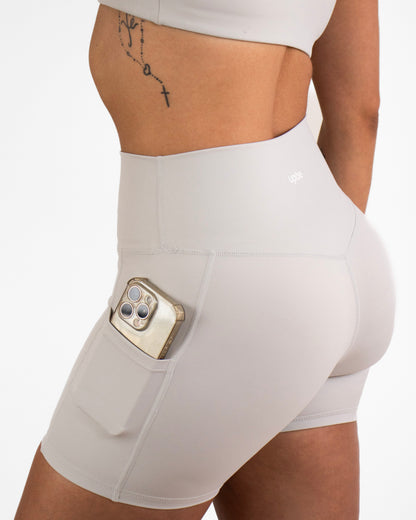 Person wearing grey high-waisted shorts with a pocket holding a phone on a plain background
